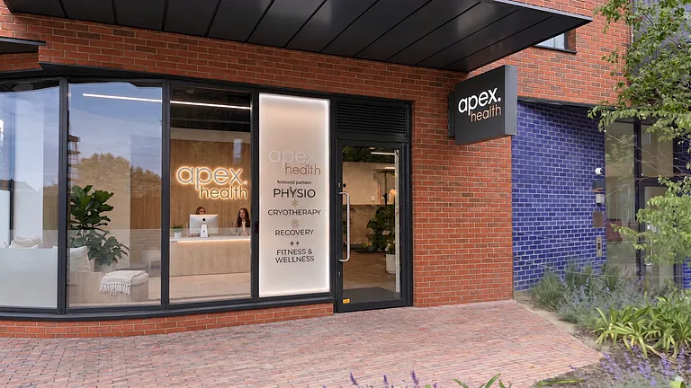 Brick-fronted Apex Health clinic entrance with glazed doors and a lit logo sign