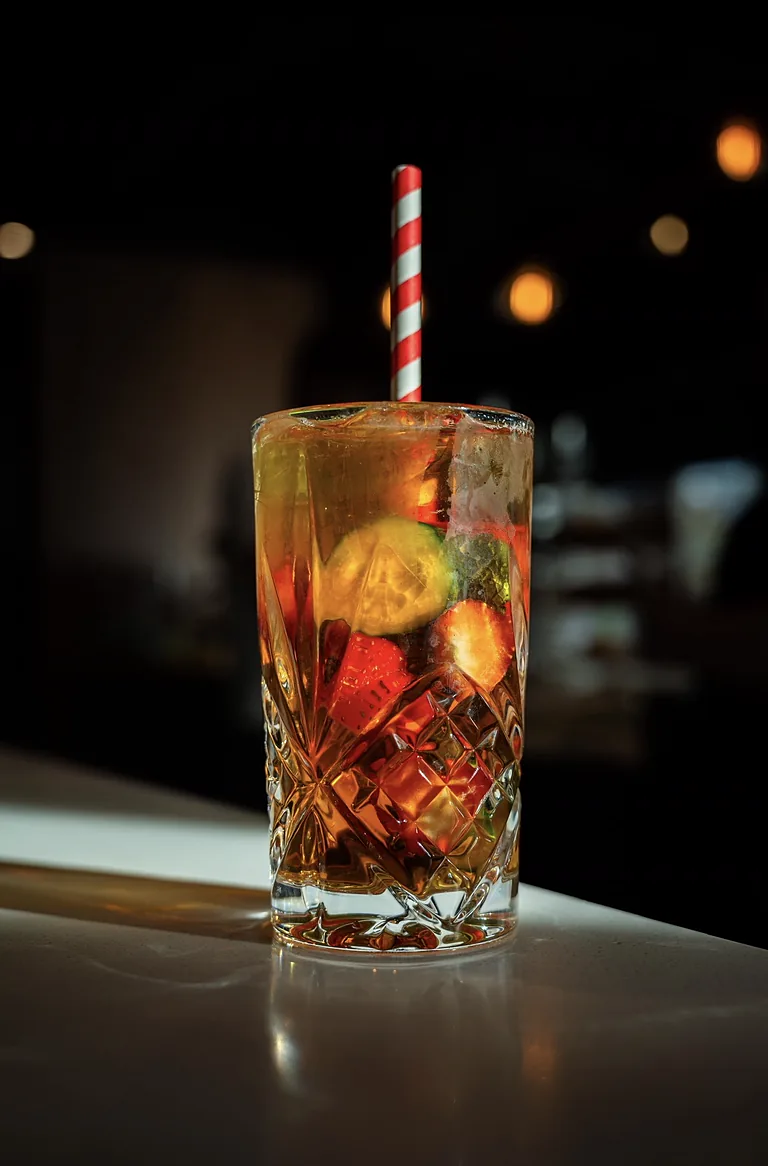Iced drink with a cucumber slice and a red-and-white striped straw on a café bar