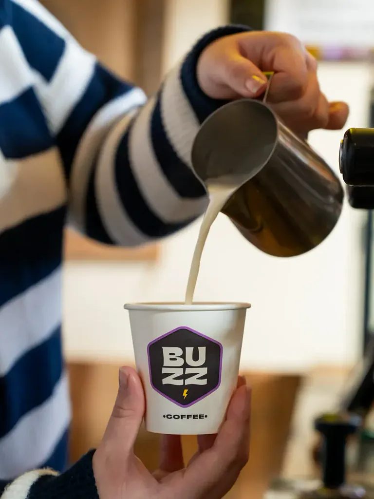 Milk being poured from a steel jug into a takeaway coffee cup