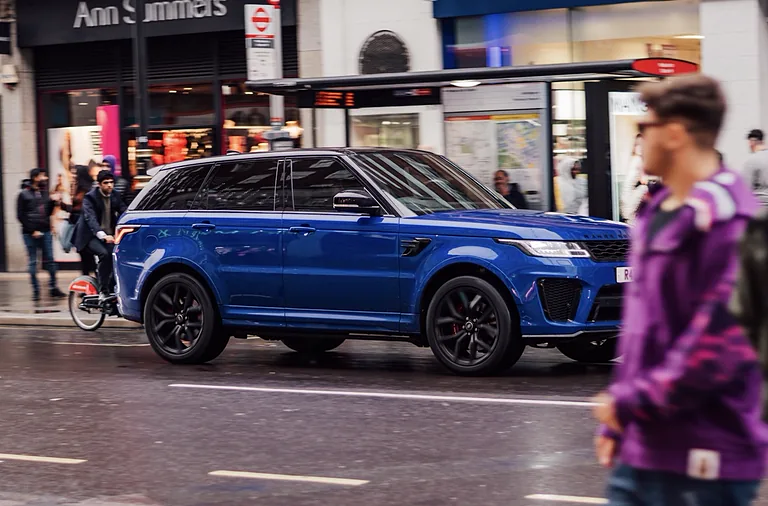 Blue Range Rover on a busy London high street as a pedestrian in a purple jacket walks past