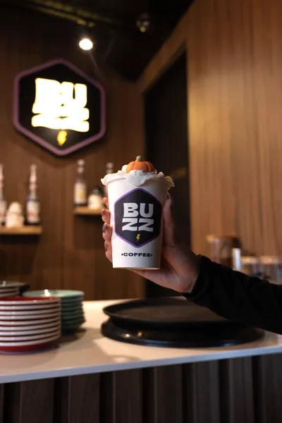 Cream-topped autumn drink in a Buzz Coffee cup, held up at the café counter